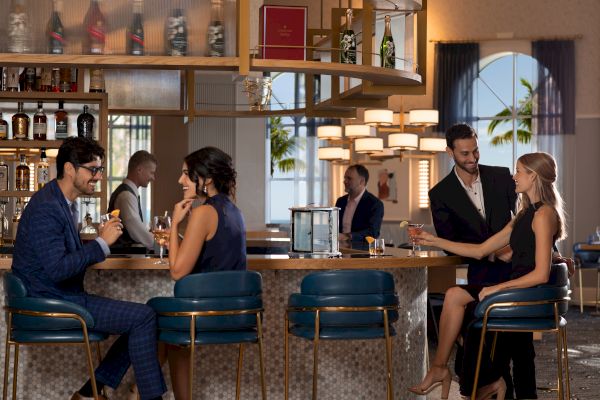 People are socializing at a stylish bar, enjoying drinks, dressed in elegant attire.