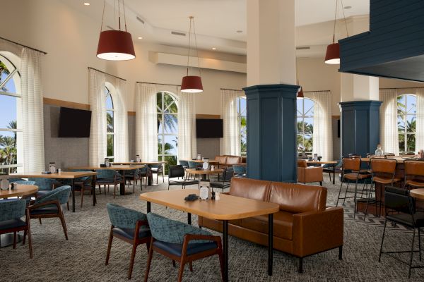 A spacious, modern dining area with tables, chairs, large windows, sofas, and hanging lights, offering a relaxed ambiance.