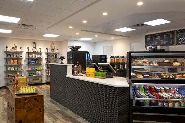 The image shows a modern coffee shop interior with a display of pastries, beverages, and snacks, alongside a counter with registers.
