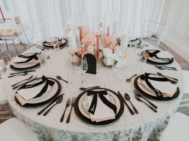 Elegant table setting with floral centerpiece, candles, and black-ribboned menus. Plates and glasses arranged around a white tablecloth.