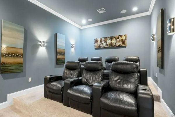 A home theater room with black leather recliners, paintings on the walls, and dim lighting.