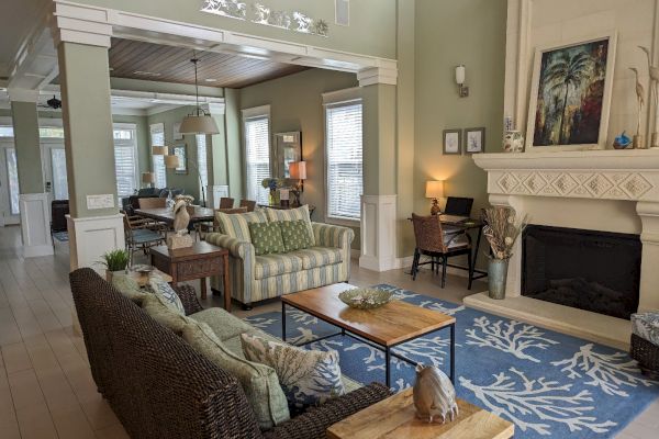 A living room with wicker furniture, coastal decor, a fireplace, and artwork. Soft lighting adds warmth, with a desk area in the corner.