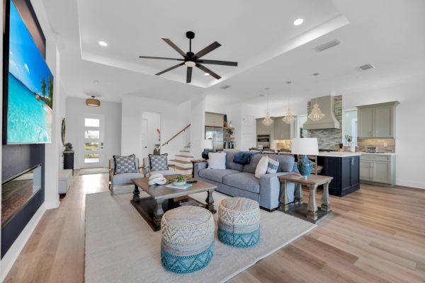 A modern living room and kitchen with a large TV, cozy seating, poufs, pendant lighting, and a wooden floor.