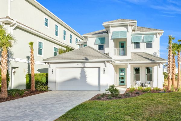 A modern two-story house with a garage, palm trees, and green lawn under a clear blue sky.