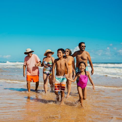 A group of people is walking on a sunny beach, enjoying the ocean and summer vibes.